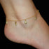 A person's ankle features a captivating anklet from the Owl Charms collection, filled with wisdom and intuition. It is delicately adorned with small dangling hearts as lucky charms against a black background.